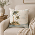 A square throw pillow with a tropical beach print featuring two palm trees on a small island, resting on a beige armchair with a knitted cream throw blanket.