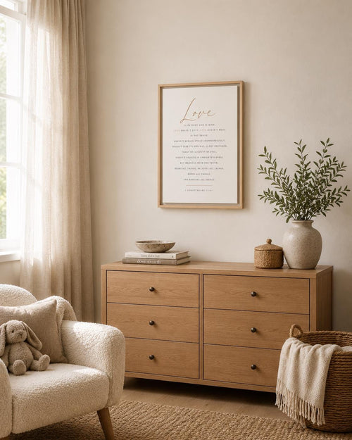 A styled interior scene showing a light wood six-drawer dresser against a warm beige wall, with a framed print above, a vase of greenery, books, and a throw blanket draped over an armchair in a softly lit room.