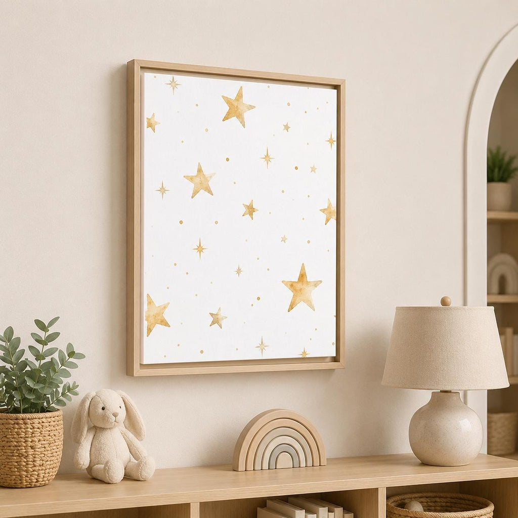 A framed wall art print featuring a white background with scattered gold watercolor stars, displayed in a styled nursery or children's room above a wooden shelf with a lamp, bunny toy, and plant.