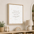 A framed wall art print with a Bible verse and small gold stars, displayed in a styled nursery setting above a wooden shelf with a lamp, bunny toy, and plant.