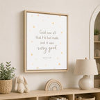 A framed wall art print with a Bible verse and small gold stars, displayed in a styled nursery setting above a wooden shelf with a lamp, bunny toy, and plant.