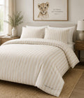A neatly made bed in a softly styled bedroom, featuring a cream and beige striped duvet cover and matching pillow shams. The brand name 'THEO & CO.