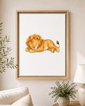 A framed watercolor art print of a sleeping golden lion, displayed on a light beige wall in a styled living room setting with a sofa, lamp, and potted plant.