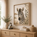 A framed art print of a zebra with Safari botanical details hangs on a beige wall above a wooden dresser in a styled room setting.