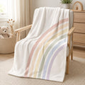 A soft white throw blanket with pastel rainbow stripes draped over a wooden armchair in a bright, neutral nursery or playroom setting.