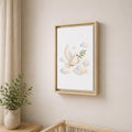 A framed wall art print hangs on a beige wall above a wooden crib, showing a white dove carrying an olive branch among soft pastel clouds. The frame is light wood, and a small potted plant and curtain are visible in the room.