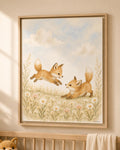 A framed art print depicting two playful foxes in a meadow of wildflowers under a cloudy sky, styled on a beige wall above a wooden crib.