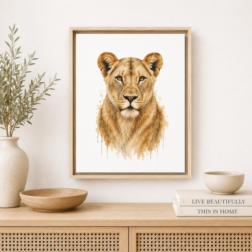 A framed watercolor art print of a lioness face, displayed on a light wood console table in a styled room setting with a vase, bowls, and books.