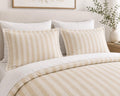 A neatly made bed with a cream and beige striped duvet cover and matching pillow shams, styled in a bright, neutral bedroom setting.