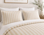 A neatly made bed with a cream and beige striped duvet cover and matching pillow shams, styled in a bright, neutral bedroom setting.