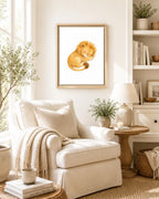 A framed watercolor art print of a sleeping lion cub hanging on a wall in a bright, modern living room with a cream armchair, side table, and lamp.