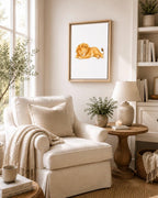 A framed art print of a sleeping lion hanging on a beige wall in a cozy, sunlit living room with a cream armchair, wooden side table, and lamp.