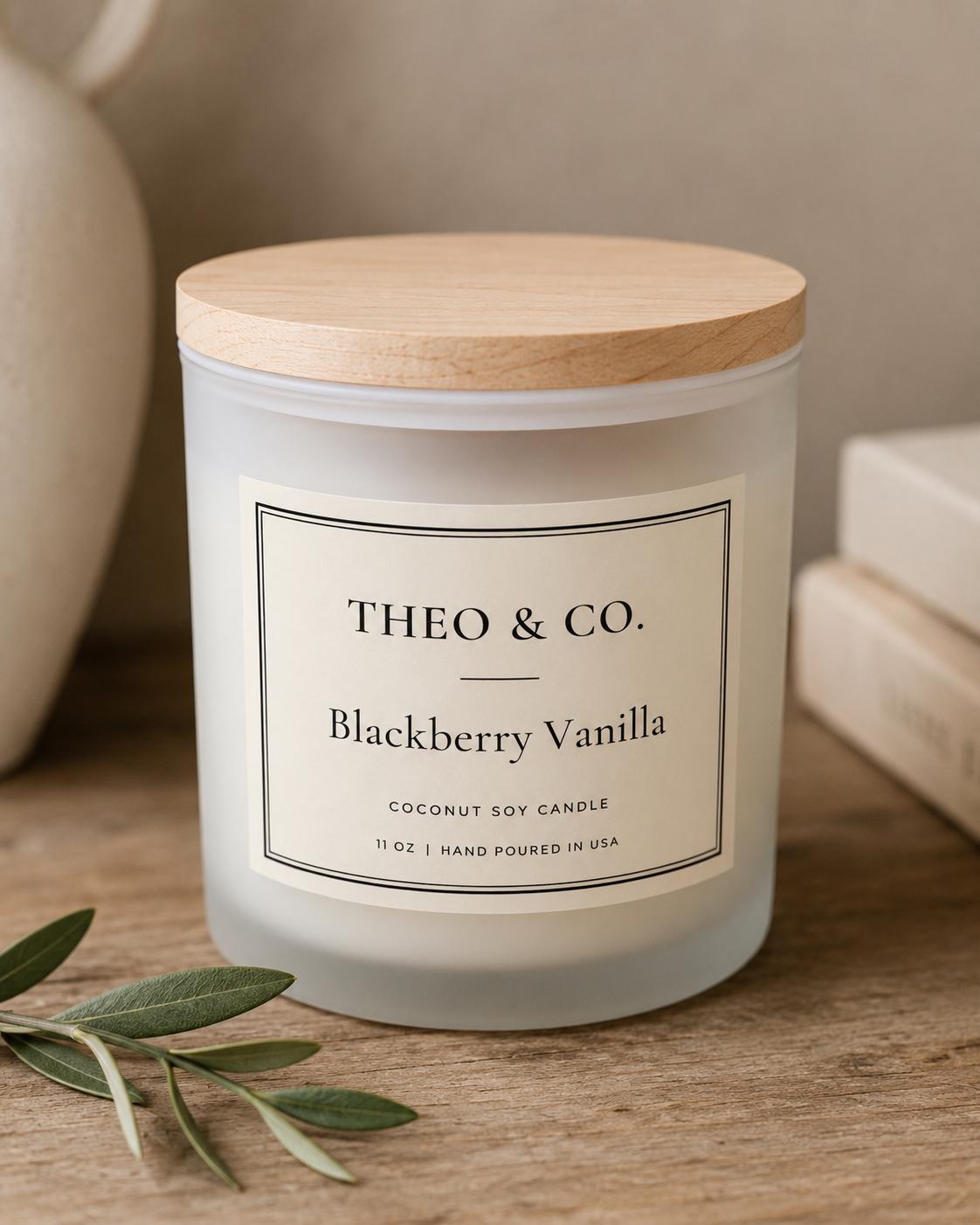 A frosted glass jar candle with a light wood lid and a cream label reading 'THEO & CO. Blackberry Vanilla'.