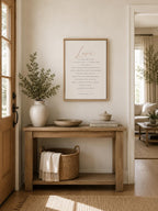 A framed vertical art print with the word 'Love' in cursive and a poem below, styled on a light wood console table in a warm, modern entryway.