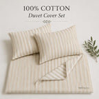 A 100% cotton duvet cover set in a cream and light beige vertical stripe pattern, featuring two pillows and a folded duvet cover, styled with a small green leaf branch on a light beige background. Text at the top reads '100% COTTON Duvet Cover Set' and the brand 'THEO.