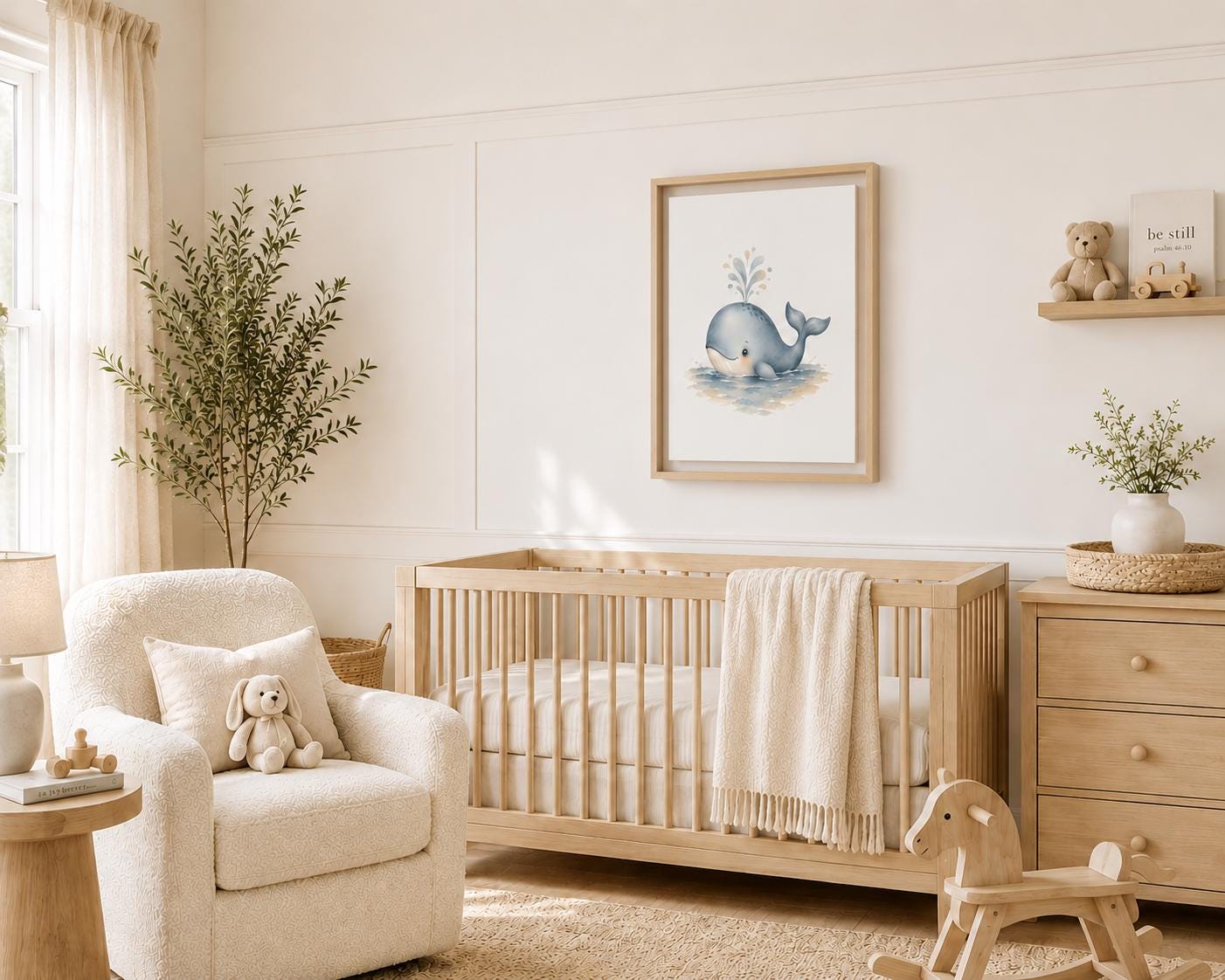 A styled nursery interior featuring a light wood crib with a cream throw blanket, a matching wooden dresser, a cream armchair with a stuffed bunny, and a framed whale art print on the wall.