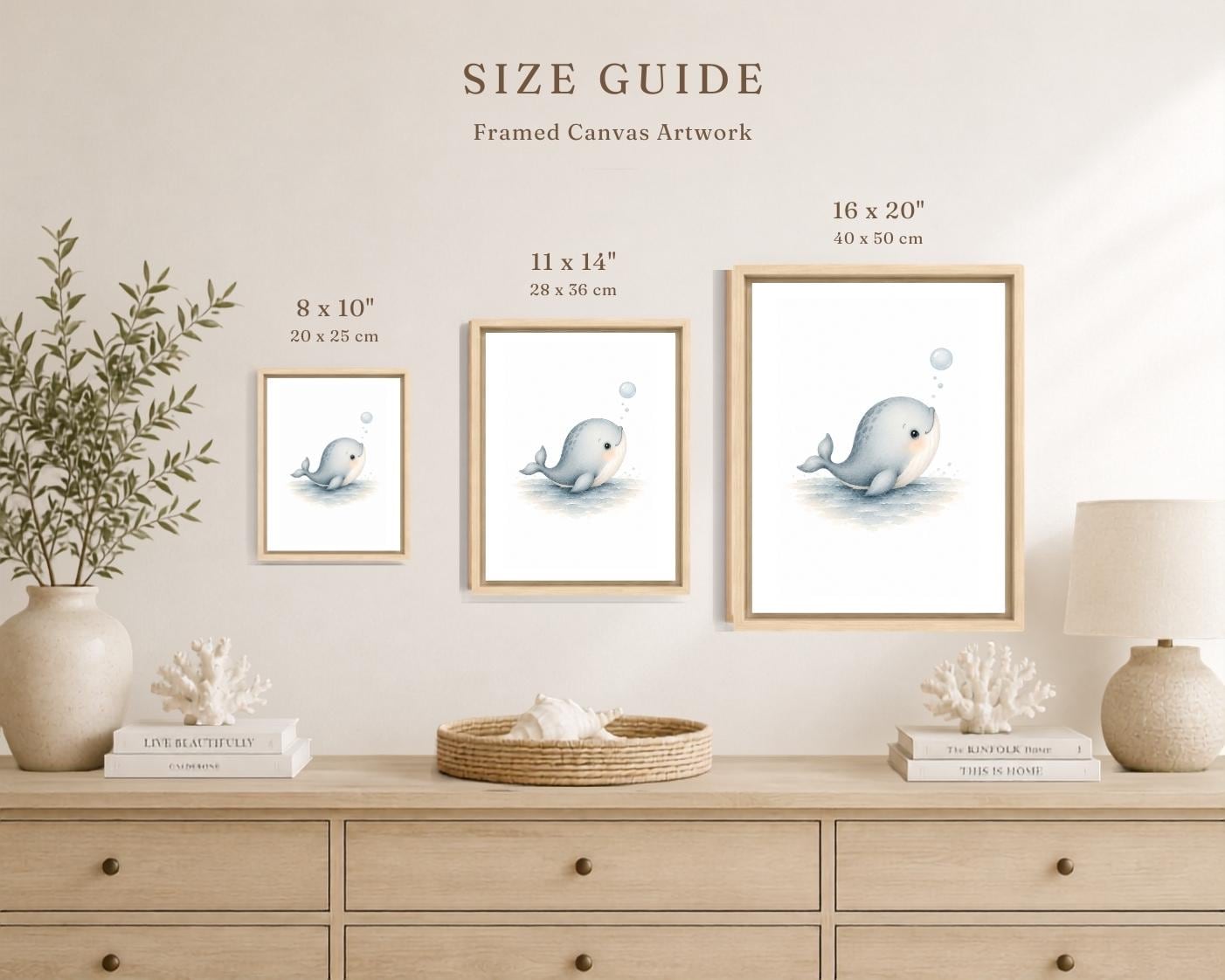 A size guide display for framed canvas wall art showing three versions of a whale illustration in different sizes: 8 x 10 inches, 11 x 14 inches, and 16 x 20 inches. The frames are hung on a beige wall above a light wood dresser decorated with a vase of greenery, books, and a lamp.