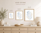 A size guide mockup showing three framed canvas art prints in different sizes (8 x 10, 11 x 14, and 16 x 20 inches) hanging on a beige wall above a light wood console table decorated with a vase of greenery, books, and a lamp.