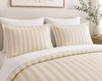 A neatly made bed with a cream and beige striped duvet cover and matching pillow shams, styled in a bright, neutral bedroom setting.