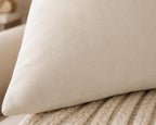 A close-up of a cream-colored faux leather or suede pillow resting on a beige ribbed knit blanket.