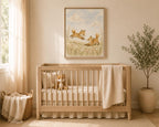 A light natural wood crib in a softly styled nursery, with a cream blanket draped over the side, a stuffed animal inside, and a framed fox painting on the wall above. A potted plant, basket, and window with warm curtains are visible in the room.