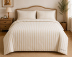 A neatly made bed in a warm, styled bedroom setting, featuring a cream and beige vertically striped duvet cover and two matching pillowcases. The brand name 'THEO & CO.