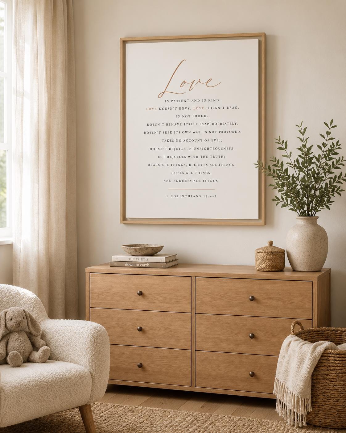 A framed art print featuring the word 'Love' in elegant cursive and a poem below in serif text, displayed on a light wood dresser in a styled room with a chair, basket, and vase. A framed typographic wall art print featuring the word 'Love' in large cursive at the top and a centered Bible verse from 1 Corinthians 13:4-7 in small serif text below, shown in a thin light wood frame against a white background.