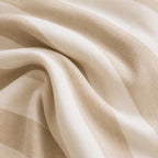 A close-up of draped beige fabric with soft folds and a subtle woven texture.