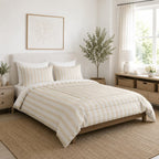 A neatly made bed in a bright, modern bedroom featuring a cream and beige striped duvet cover and matching pillow shams, set against a white wall with a wooden headboard.