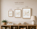 A size guide poster for framed canvas wall art, showing three framed prints of a white dove in the clouds with dimensions labeled 8 x 10", 11 x 14", and 16 x 20". The poster is displayed on a beige wall above a wooden shelf with nursery decor.
