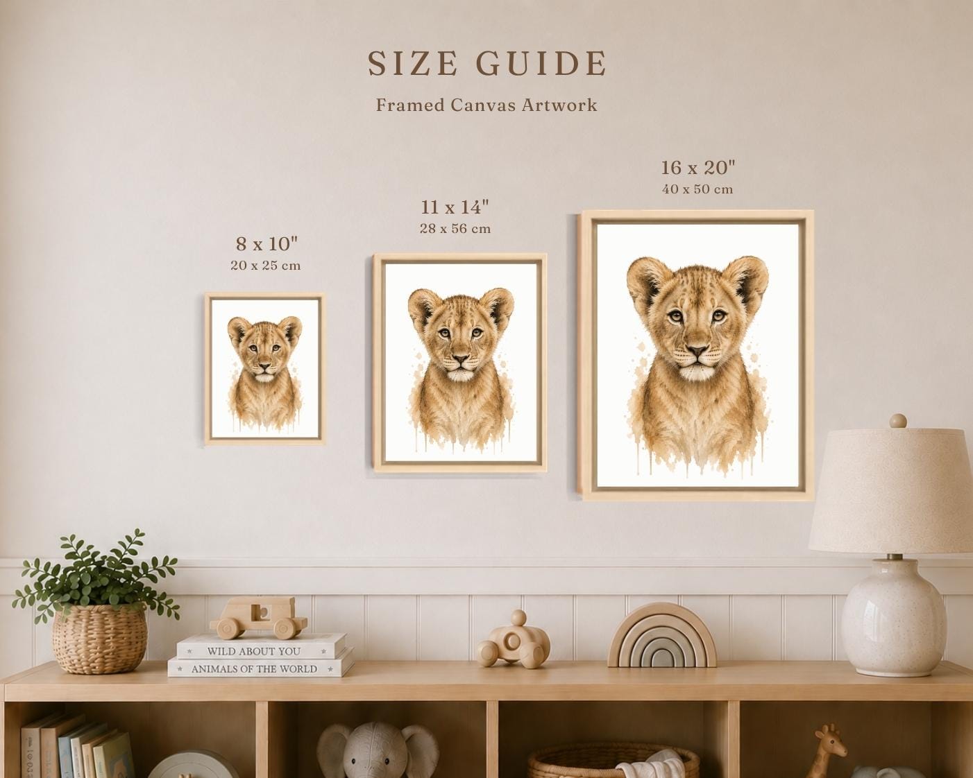 A size guide poster showing three framed canvas prints of lion cub portraits in different sizes (8 x 10, 11 x 14, and 16 x 20 inches) mounted on a beige wall above a wooden shelf with home decor.