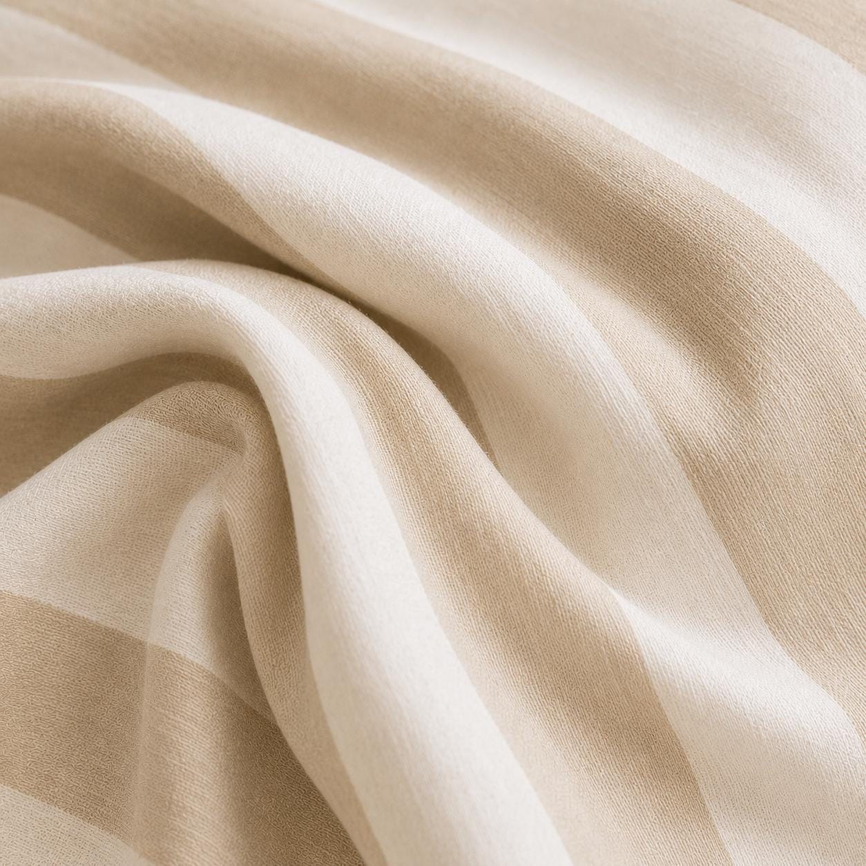 A close-up of draped beige fabric with soft folds and a subtle woven texture.