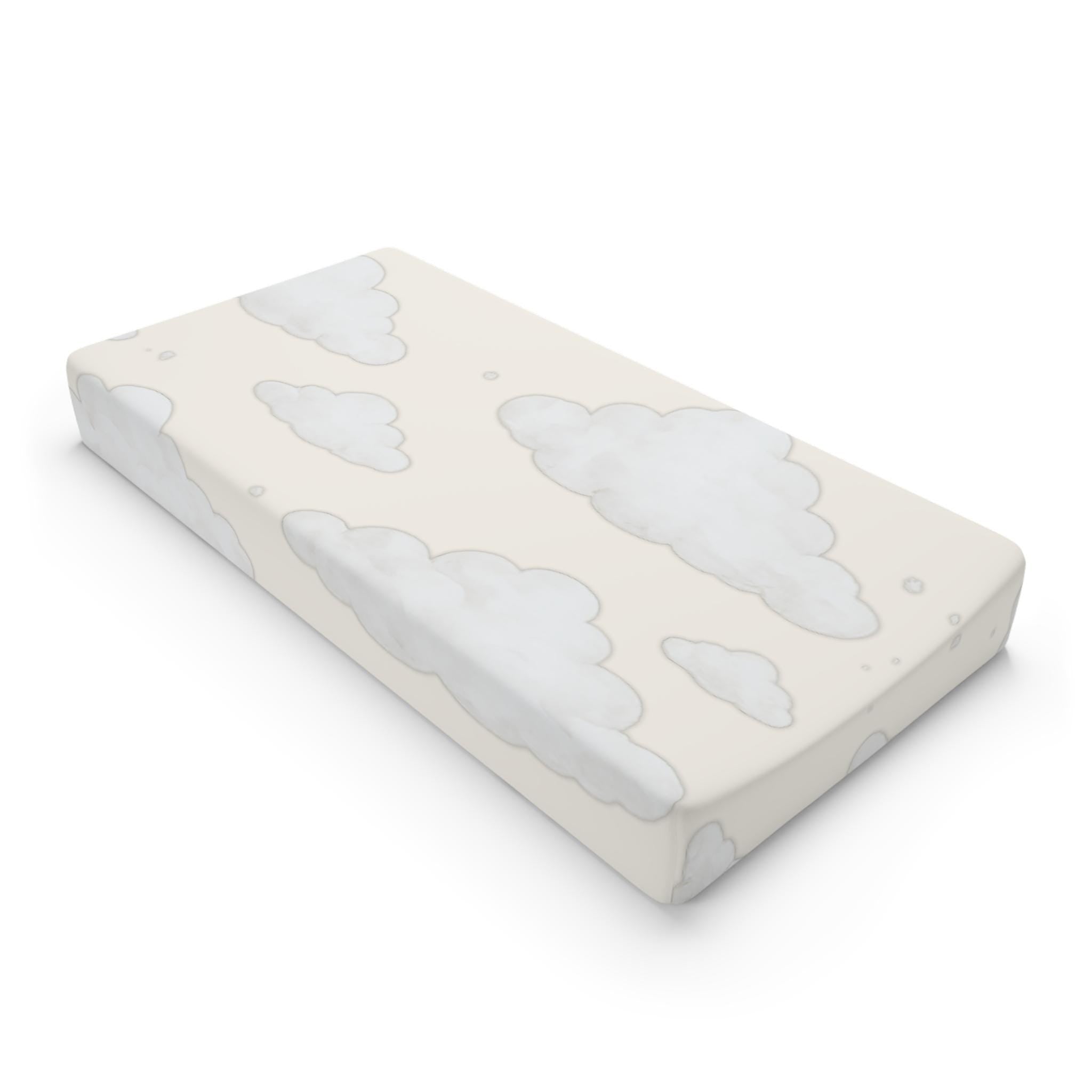 A rectangular baby mattress protector or fitted sheet with a soft cloud pattern in light gray on a warm cream background, shown at an angle on a white background.