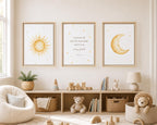 Three framed wall art prints hang above a wooden shelf in a styled nursery. The left print shows a yellow sun, the center shows a Bible verse in black script, and the right print shows a yellow crescent moon with small stars.
