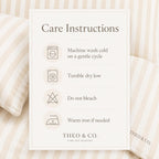 A care instructions card for Theo & Co. Timeless Bedding, displayed on a soft beige and cream striped background with pillows.