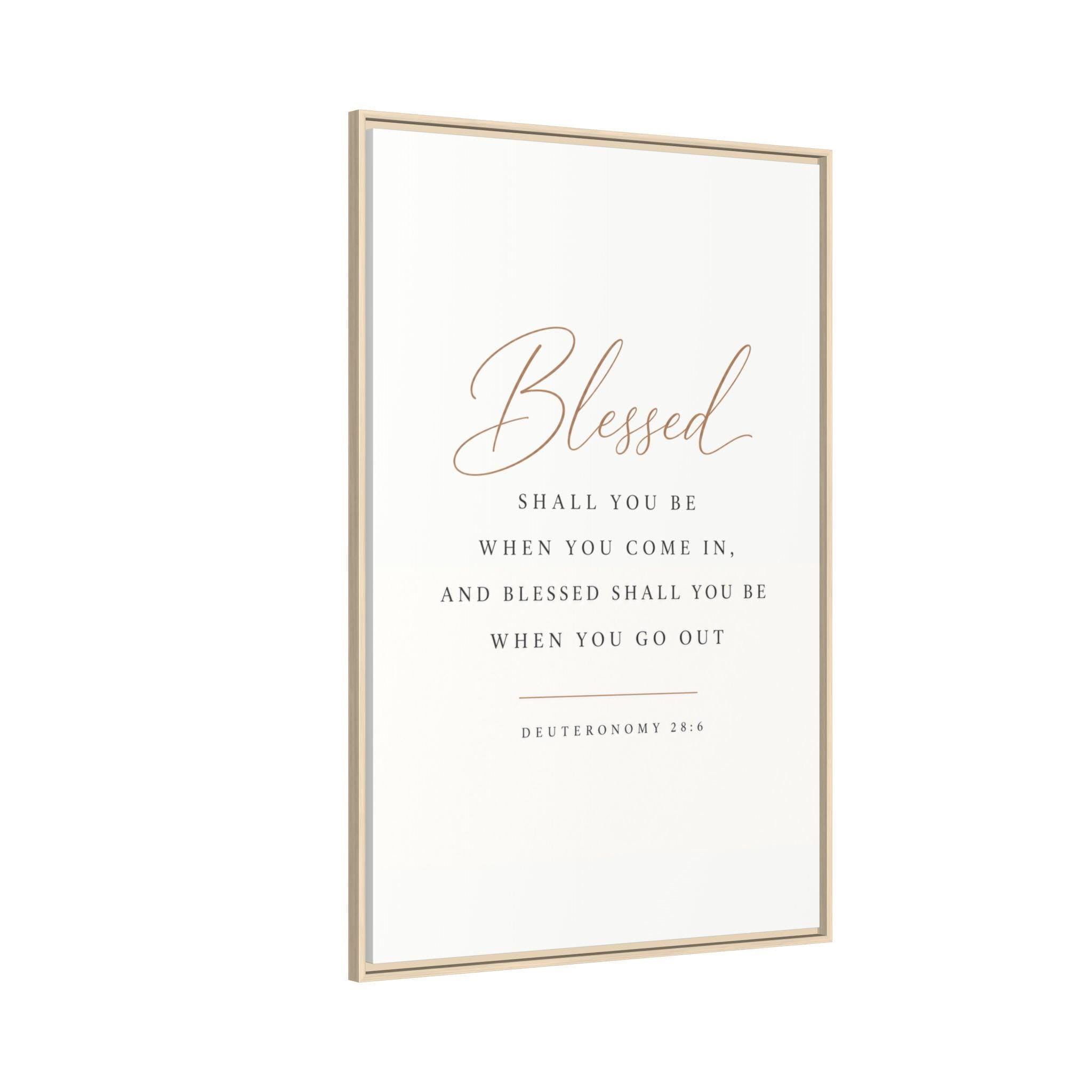 A vertical framed wall art print with a white background and a thin light wood frame. The print features the word 'Blessed' in elegant cursive, followed by the biblical quote 'Shall you be when you come in, and blessed shall you be when you go out' from Deuteronomy 28:6-7 in dark gray serif text.