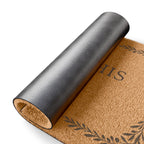 A rolled coir doormat with a dark gray protective outer cover partially peeled back, showing a natural tan coir texture and dark printed decorative motifs and lettering, on a white background.