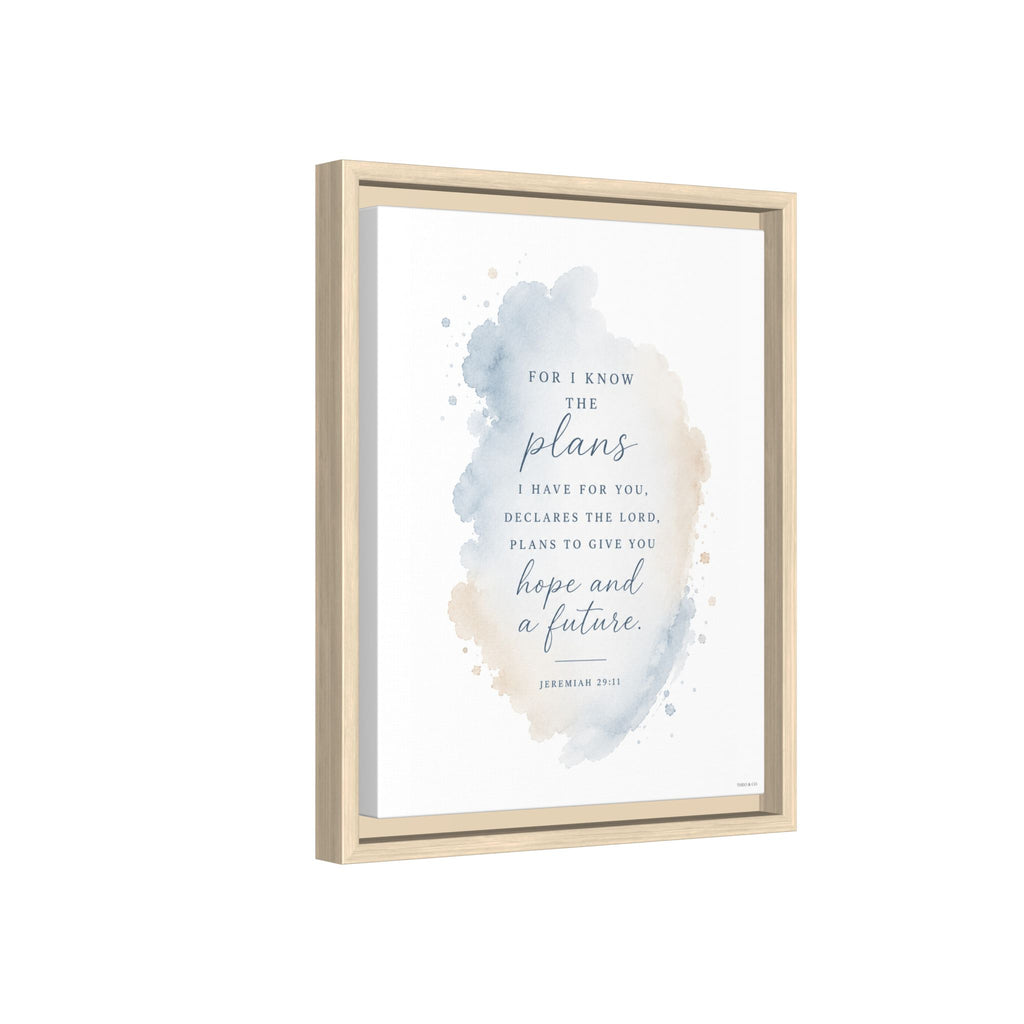 Framed wall art featuring a Bible verse in elegant black and blue script over a soft watercolor splash in blue, beige, and gray tones, shown in a light natural wood frame against a white background.