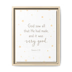 A framed wall art print featuring the Bible verse Genesis 1:31, 'God saw all that He had made, and it was very good.' The text is centered on a white background with scattered small gold stars, and the piece is housed in a light natural wood frame.