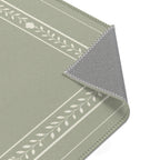 A close-up of a rectangular mat or rug with a sage green top, white leafy stripe pattern, and a gray underside showing stitched edges, photographed on a white background.