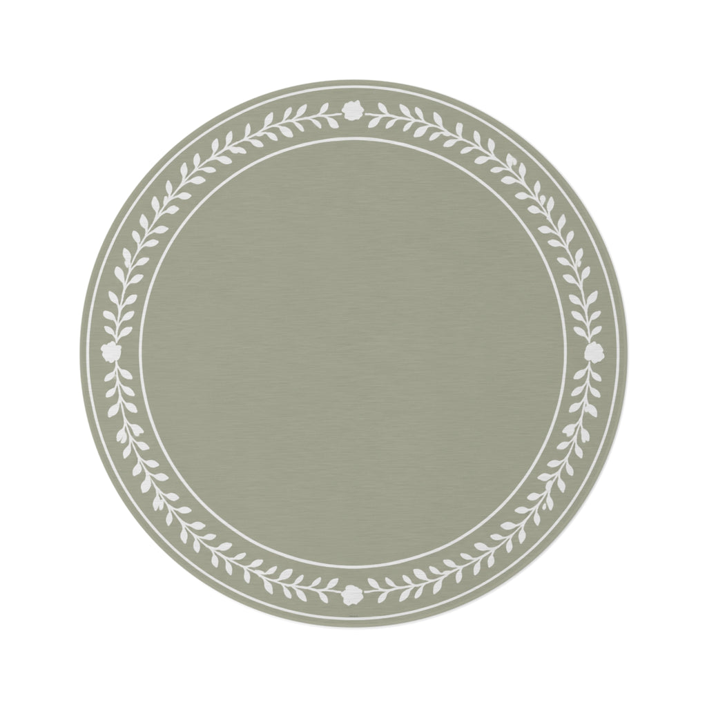 A round area rug in sage green with a white leafy floral border, styled on a white background