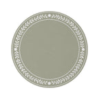 A round area rug in sage green with a white leafy floral border, styled on a white background