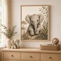 A framed art print of a baby elephant hanging on a beige wall above a wooden dresser in a safari styled nursery. The print features a detailed sepia-toned illustration of a baby elephant on a rock, flanked by leaves.