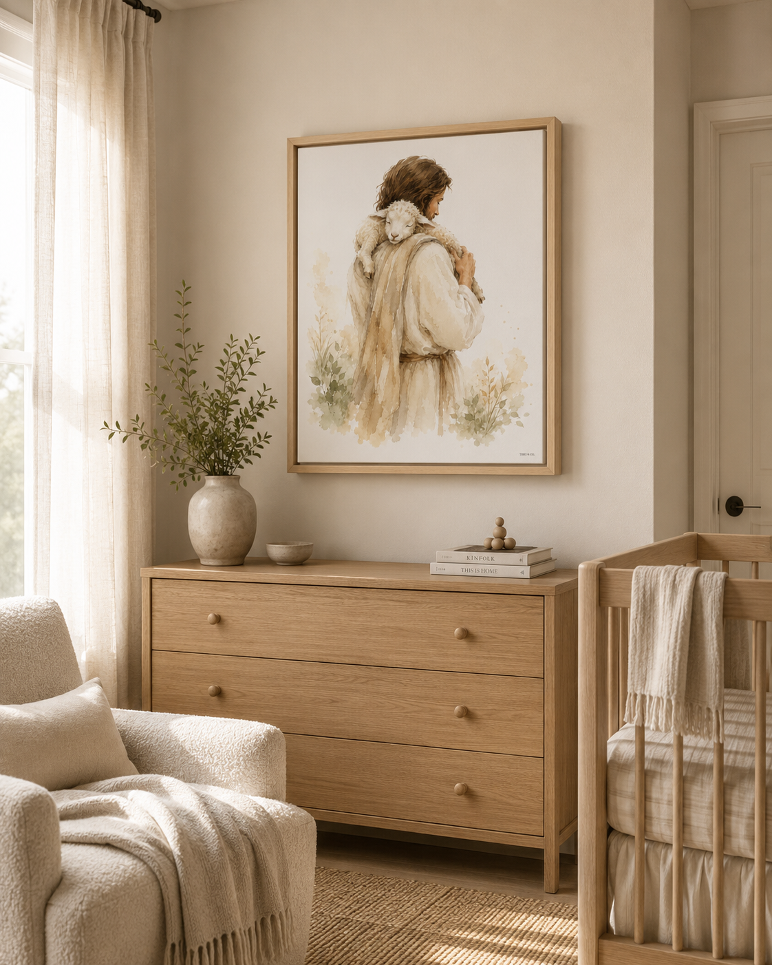 A framed art print depicting a man Jesus in a cream-colored cloak carrying a white lamb, styled on a wooden dresser table with a vase, bowl, and books in a warm, neutral-toned room.