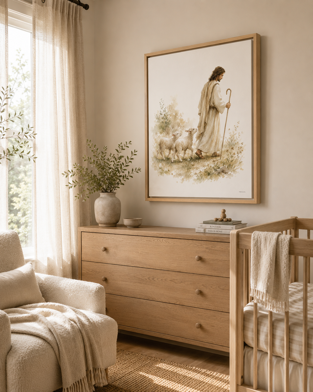 A framed art print depicting Jesus and sheep hangs on a beige wall in a softly lit nursery. The room includes a light wood dresser, a crib with a white blanket, a chair with a cream throw, and a window with sheer curtains.