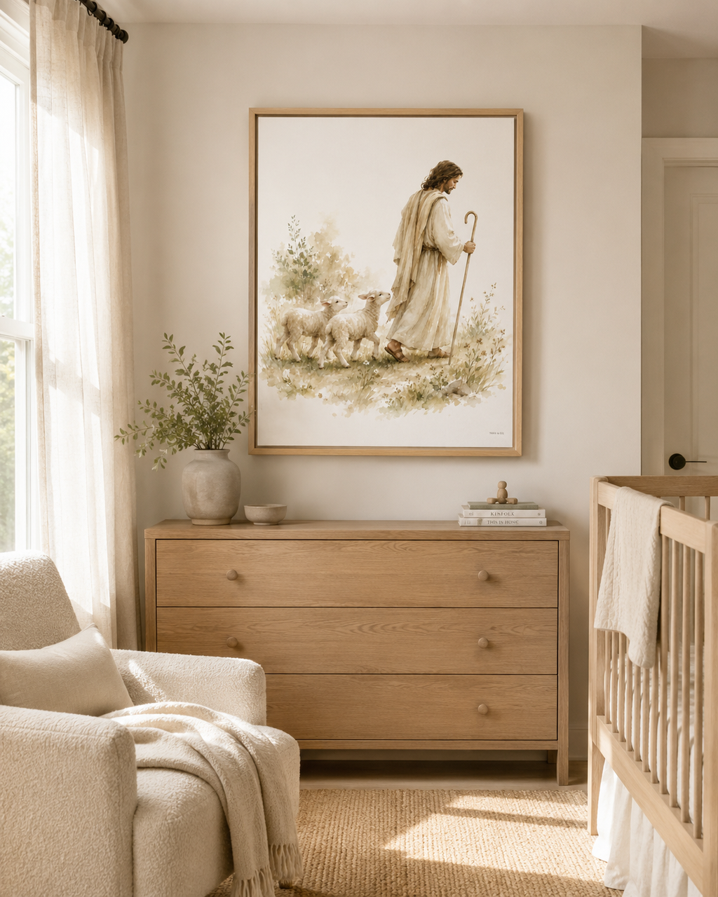 A floating Canvas in a wooden natural frame  artwork showing a man, Jesus, in white robes being a Shepherd leading two lamb behind him while holding a Shepherd's staff in a watercolor green floral field. It is styled above a dresser with a vase, a basket, with an olive tree and cream colored chair in the corner. The colors are very cream and neutral.