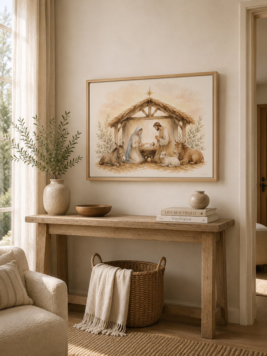 A framed nativity painting hangs on a beige wall above a rustic wooden console table in a warm, neutral-toned living room. The painting depicts Mary, Joseph, baby Jesus, and animals under a thatched stable.
