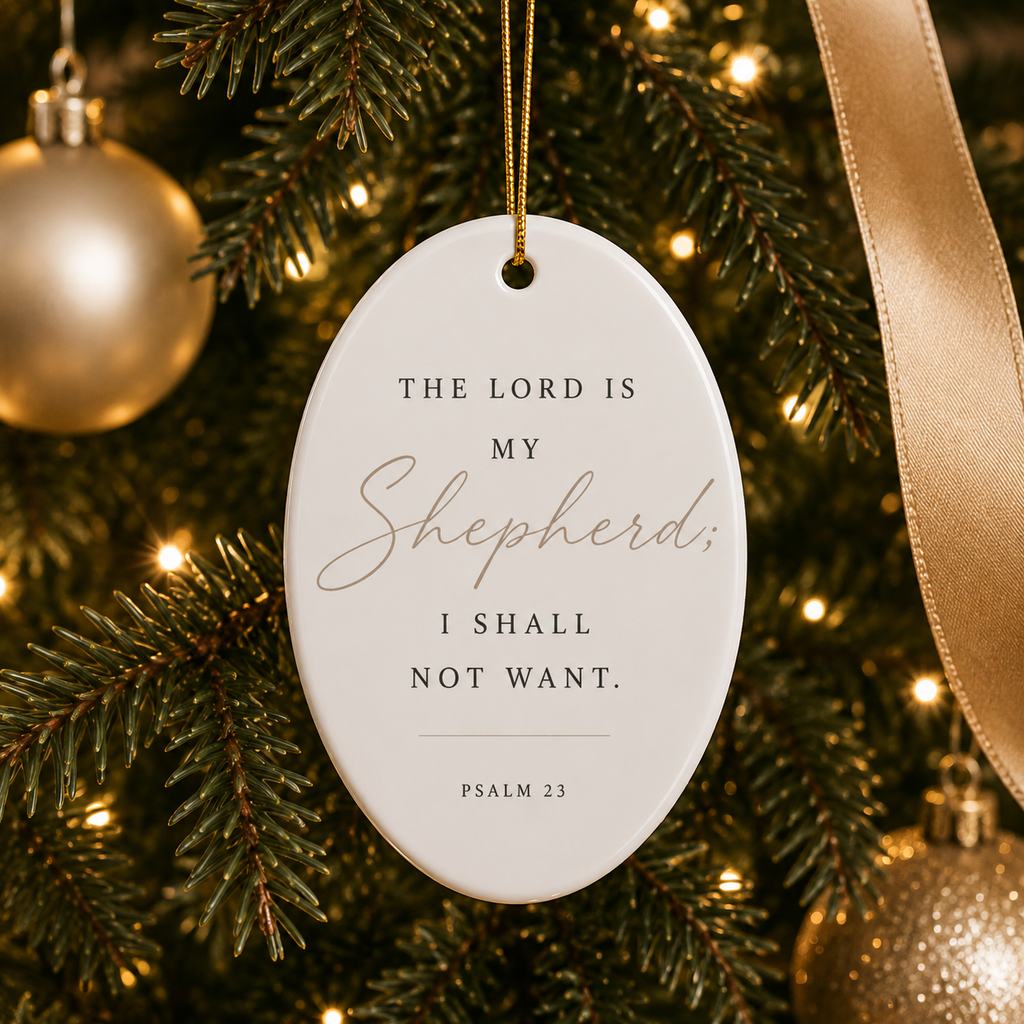 An oval white Christmas ornament hanging from a gold string on a decorated Christmas tree. The ornament features the printed text 'THE LORD IS MY Shepherd, I SHALL NOT WANT.