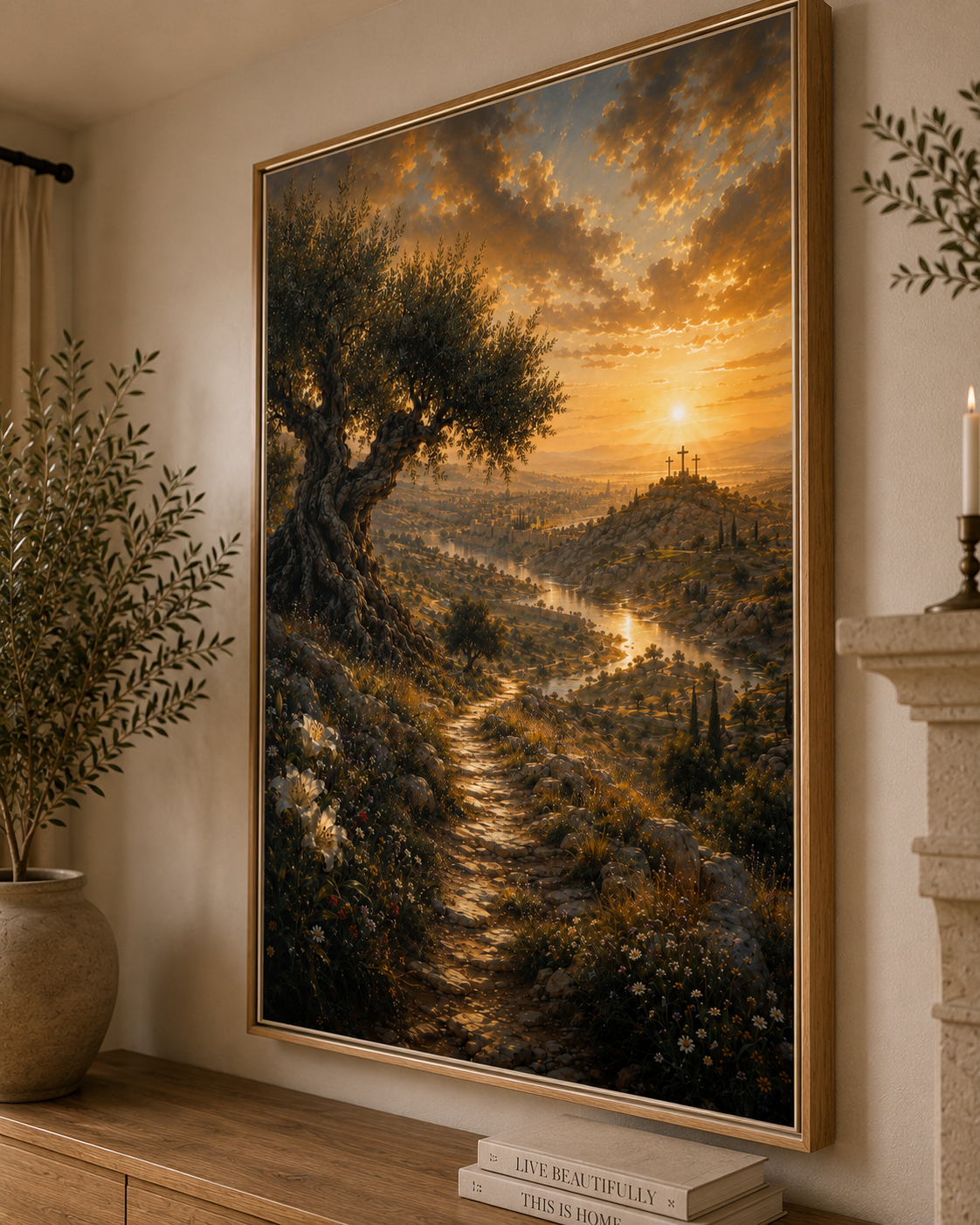 A large framed landscape painting hangs on a beige wall above a wooden console table. The artwork depicts a golden sunset over a winding path through a lush valley, with an olive tree on the left and a hilltop cross on the right.