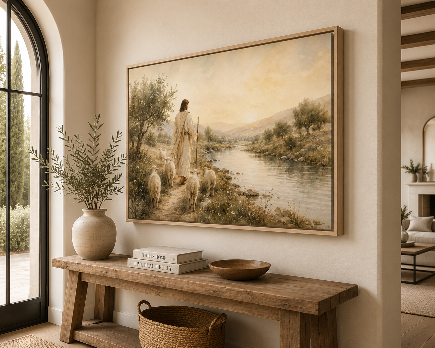 A large framed landscape painting hangs on a beige wall above a rustic wooden console table in a styled interior. The painting depicts a shepherd standing by a river with sheep in a warm, soft-focus scene.